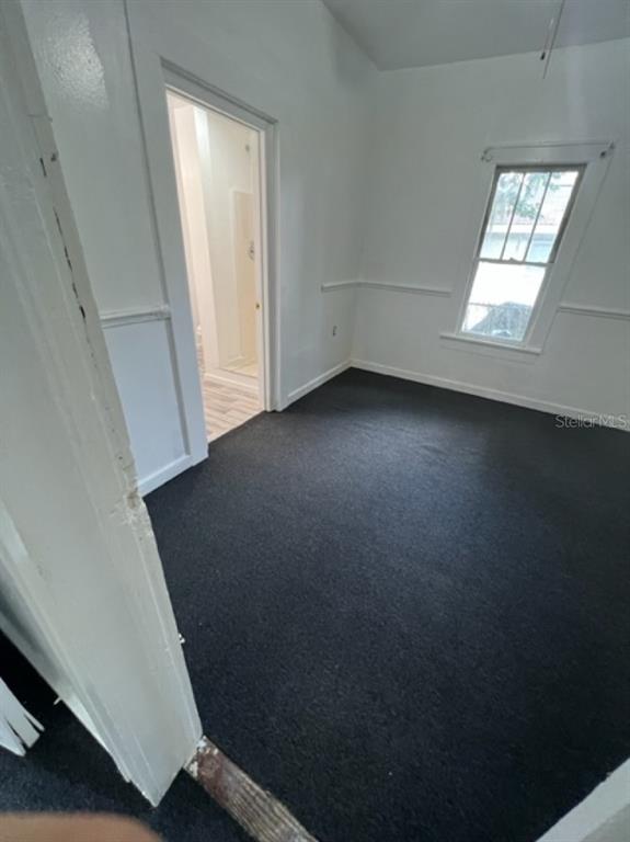 A bedroom with dark carpeting, white walls, a chair rail, and a doorway to a bathroom — 1031 N FLORENCE AVENUE, LAKELAND, FL
