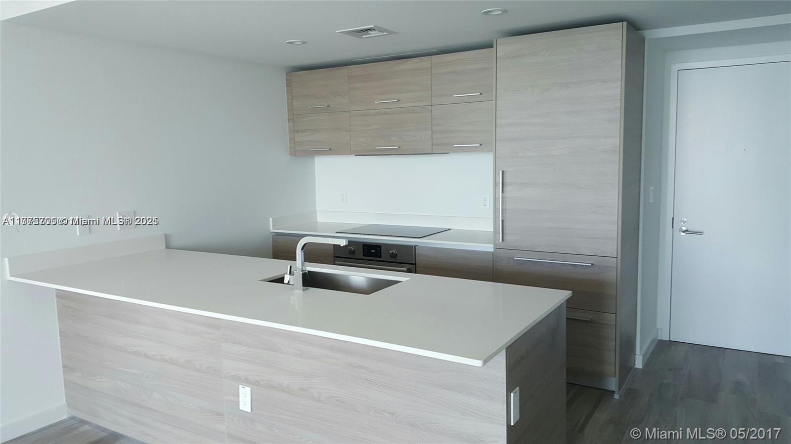 A modern kitchen features light wood cabinetry, a white countertop island, and stainless steel appliances — 1300 S Miami Ave # 4002, Miami FL 33130, MIAMI, FL