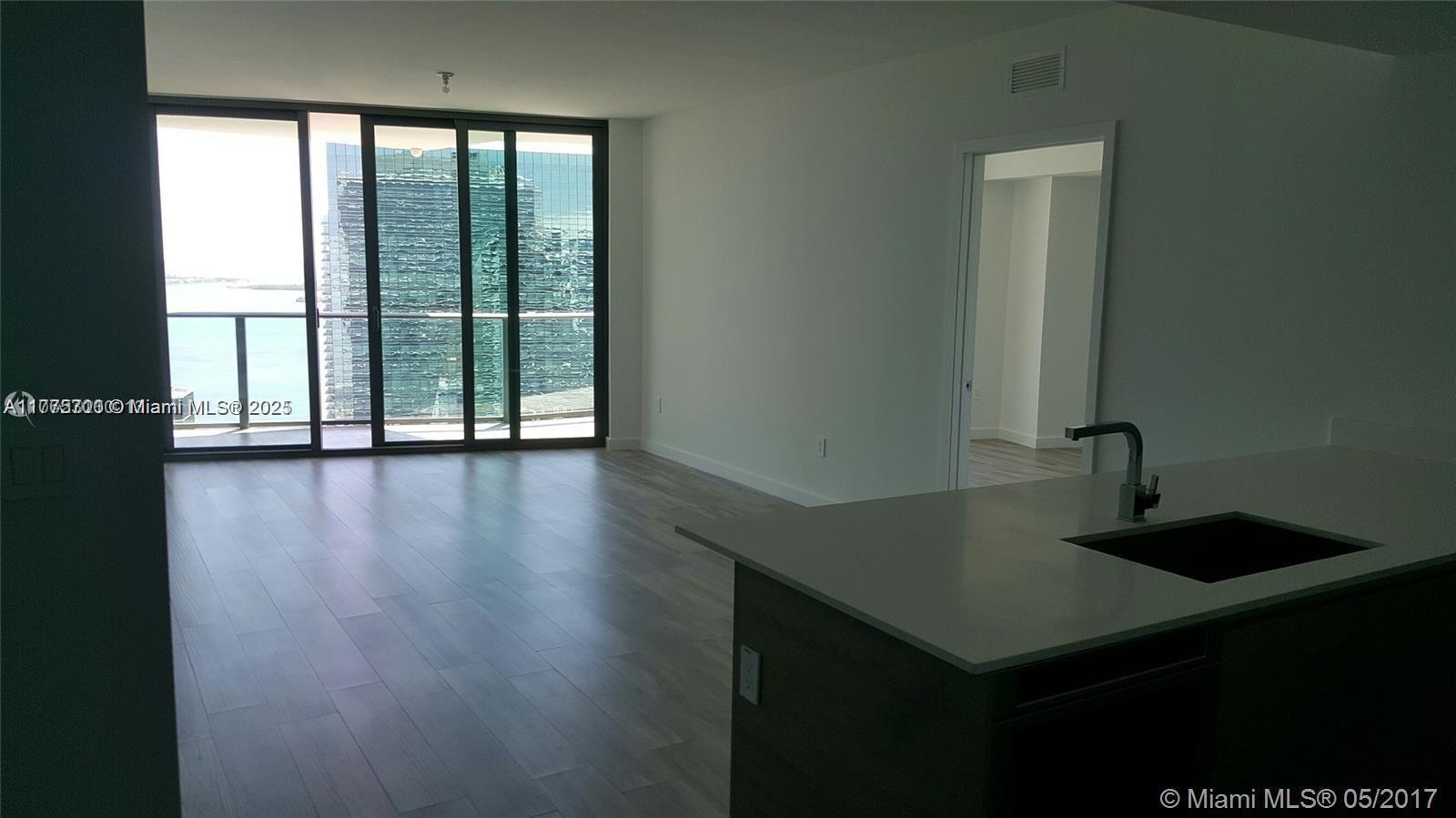 An interior view of an apartment featuring a kitchen island, light wood flooring, and balcony access — 1300 S Miami Ave # 4002, Miami FL 33130, MIAMI, FL