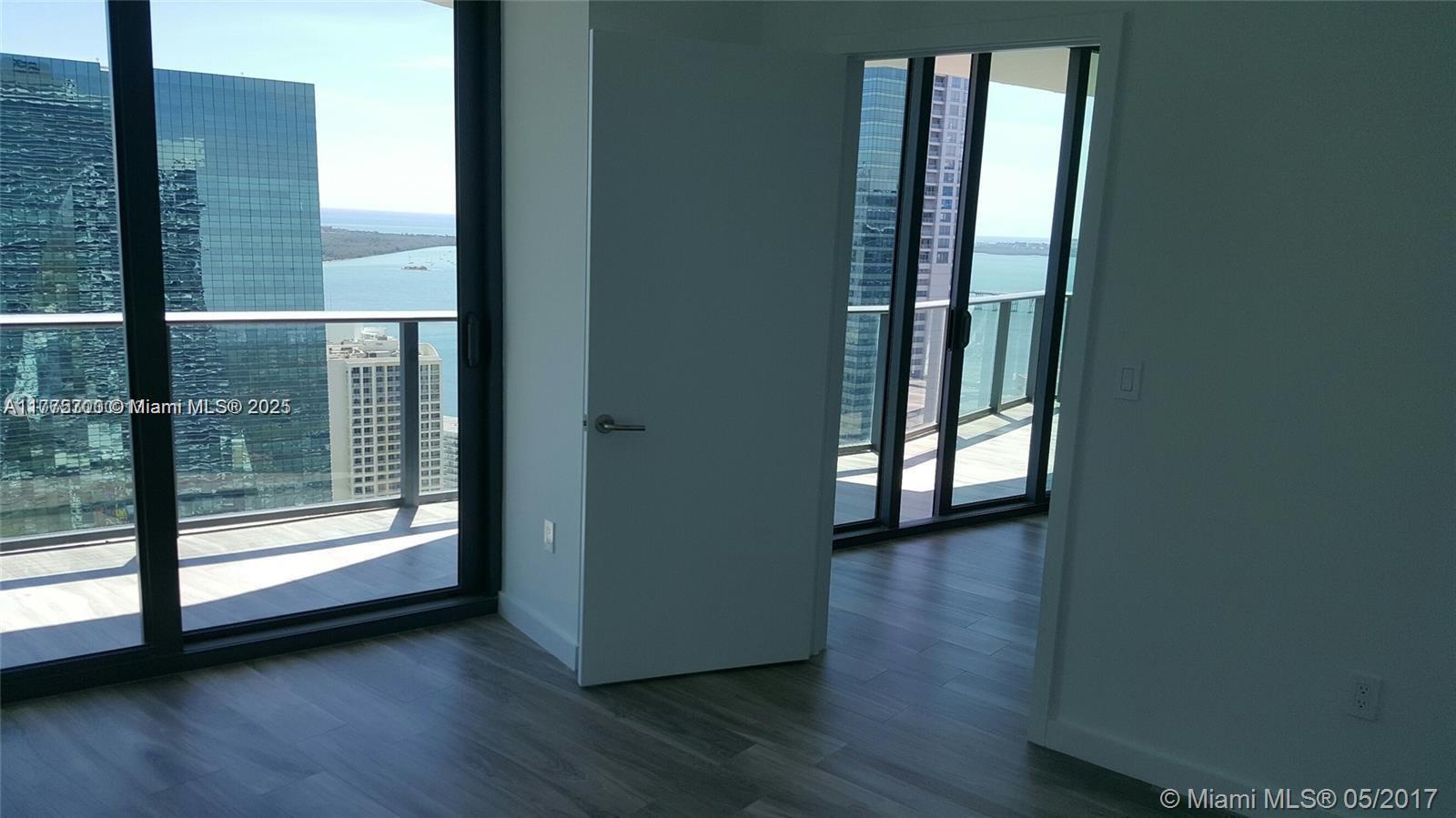 An interior room features light wood-look flooring, a white door, and floor-to-ceiling windows overlooking water — 1300 S Miami Ave # 4002, Miami FL 33130, MIAMI, FL