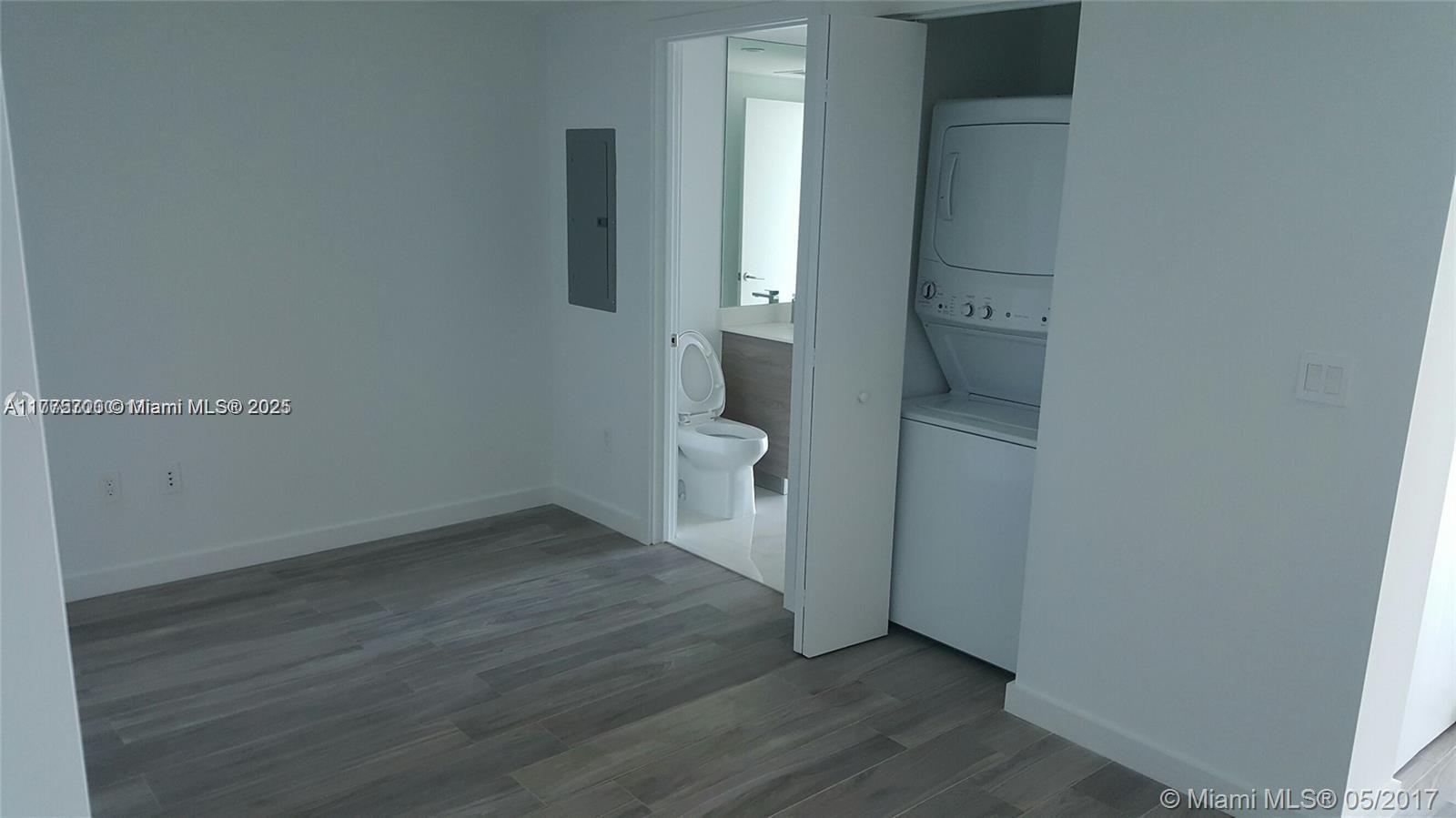 A room with wood-look flooring features a bathroom doorway and a stacked laundry unit — 1300 S Miami Ave # 4002, Miami FL 33130, MIAMI, FL
