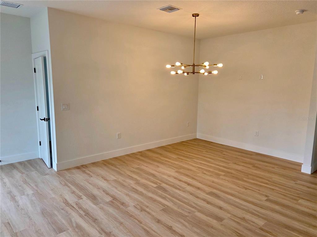 An empty dining room features light wood-look flooring, white walls, and a modern chandelier — 138 INGRAM BOULEVARD, ROTONDA WEST, FL