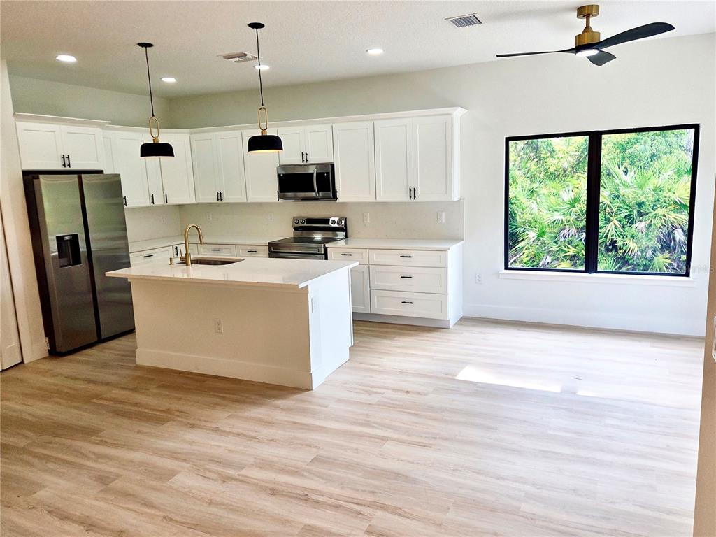 A modern kitchen features white cabinetry, a central island, stainless steel appliances, and light flooring — 138 INGRAM BOULEVARD, ROTONDA WEST, FL