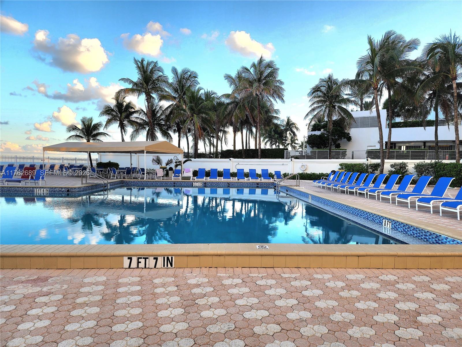 A swimming pool with lounge chairs and palm trees under a blue sky — 3505 S Ocean Dr # 819, Hollywood FL 33019, HOLLYWOOD, FL