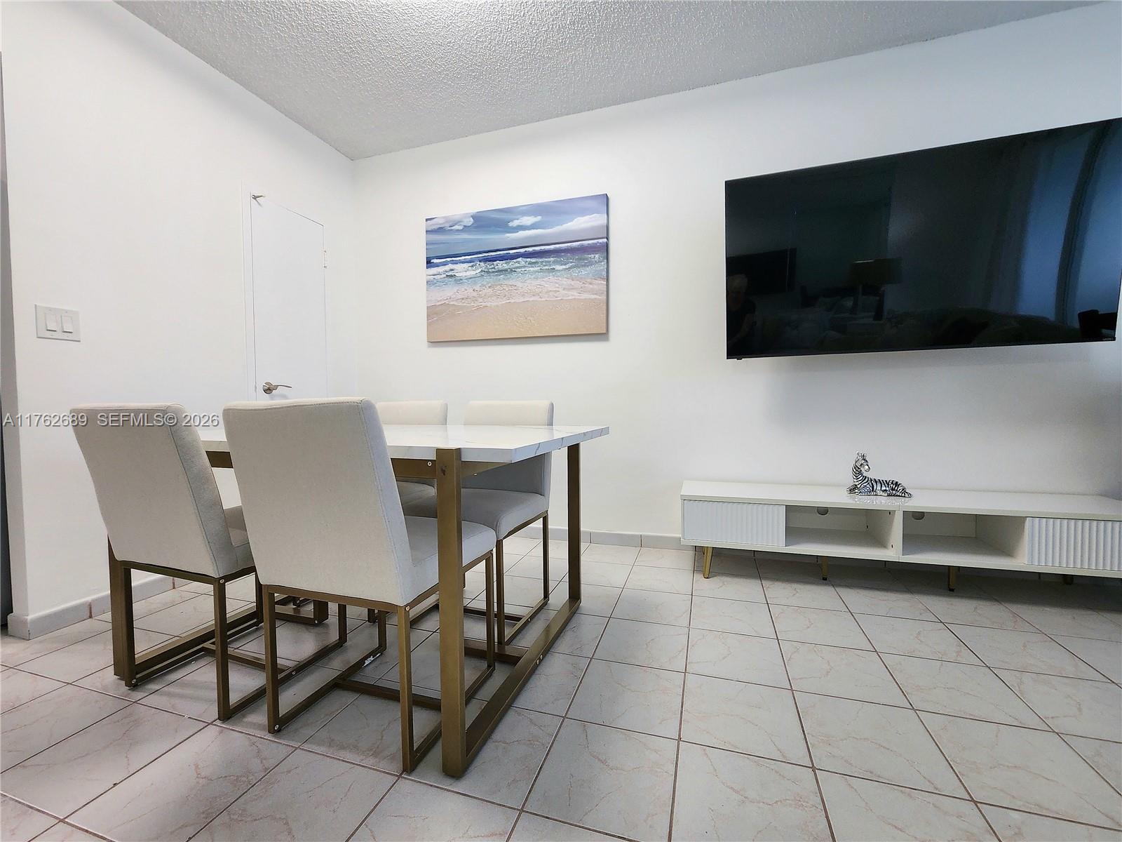 A dining area features a white table with gold legs, four chairs, and a wall-mounted television — 3505 S Ocean Dr # 819, Hollywood FL 33019, HOLLYWOOD, FL