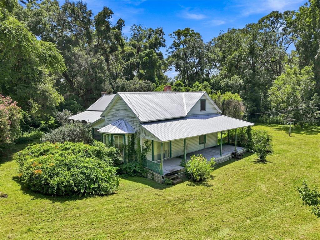 An old white farmhouse with a metal roof and a wrap-around porch sits on grass — 459 SW BIGFOOT COURT, FORT WHITE, FL