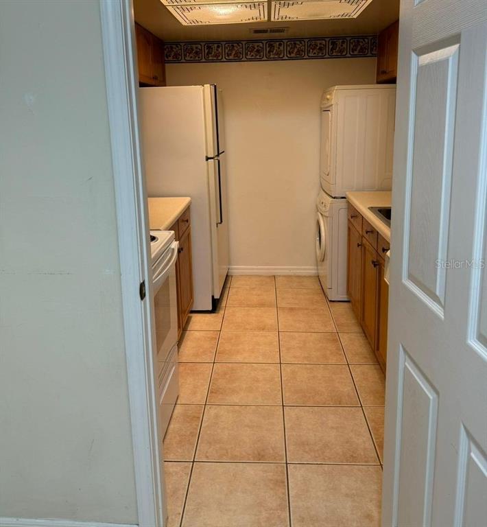 A galley-style kitchen features white appliances, wooden cabinets, and beige tile flooring — 700 E AIRPORT BOULEVARD UNIT B7, SANFORD, FL