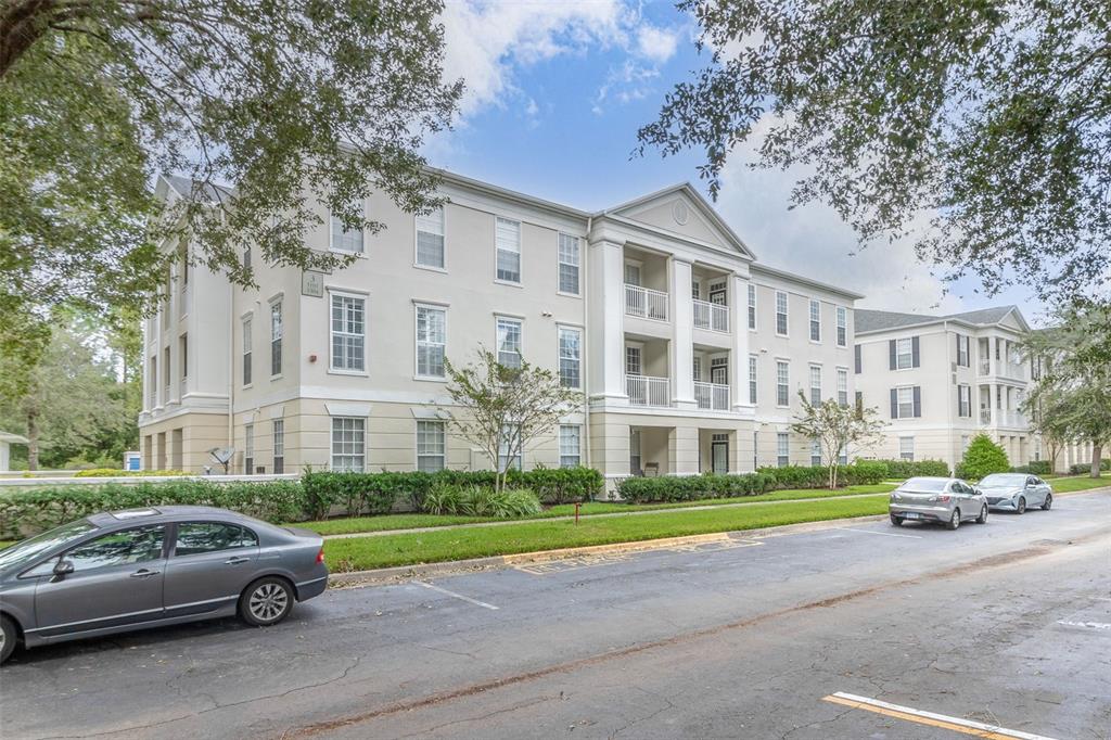 A multi-story apartment building with a beige facade and balconies sits beside a parking lot — 233 GOLDENRAIN DRIVE UNIT 202, CELEBRATION, FL