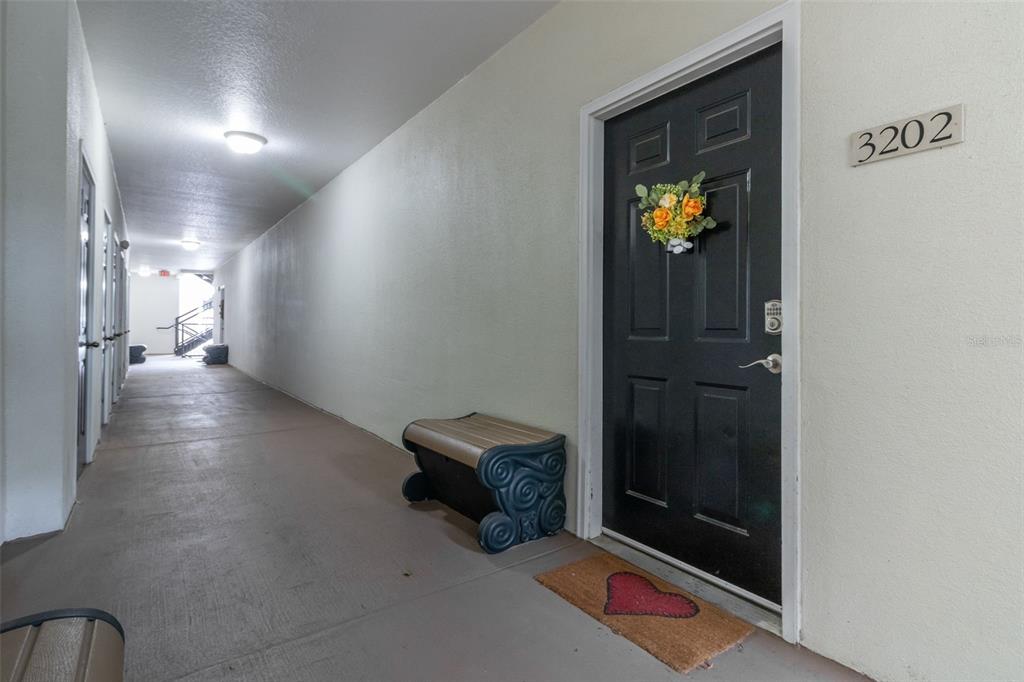 A black front door with a floral wreath and heart mat sits in an apartment hallway — 233 GOLDENRAIN DRIVE UNIT 202, CELEBRATION, FL