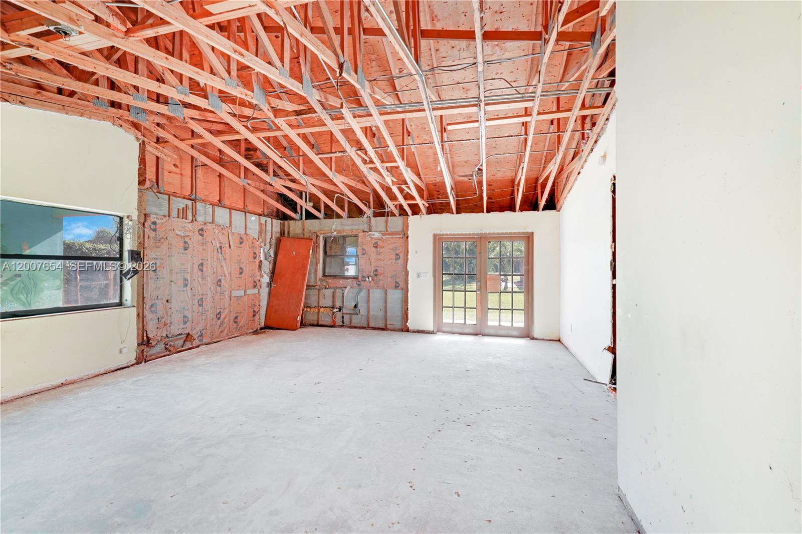 An unfinished room features exposed wooden ceiling trusses, bare concrete floors, and exposed wall insulation — 20000 SW 216th St, Miami FL 33170, MIAMI, FL