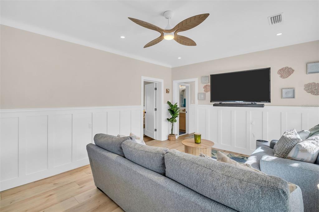 A living room features a gray sofa, white wainscoting, a ceiling fan, and a wall-mounted television — 16613 GULF BOULEVARD, NORTH REDINGTON BEACH, FL