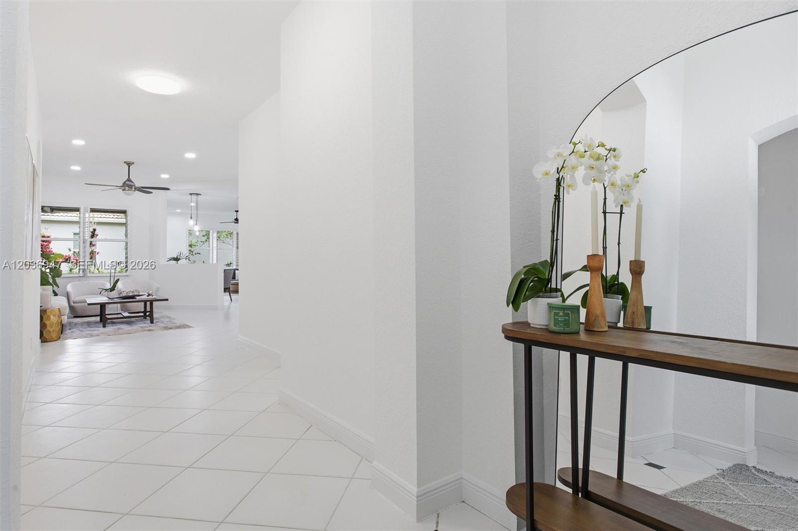 A bright hallway with white tile floors leads to a living area with a ceiling fan — 19308 Stonebrook St, Weston FL 33332, WESTON, FL