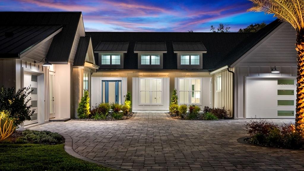 A modern farmhouse with a paved driveway, white siding, and a dark metal roof at dusk — 825 PHEASANT RUN COURT W, PORT ORANGE, FL