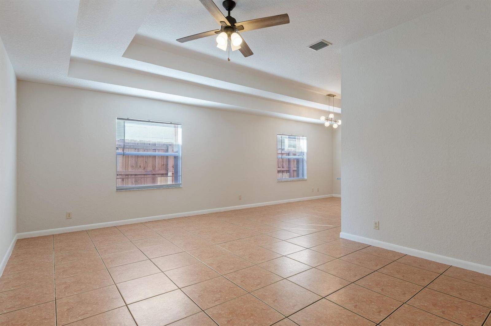 An empty room with beige tile flooring, a tray ceiling with a fan, and two windows — 623 N L Street, FL 33460, FL