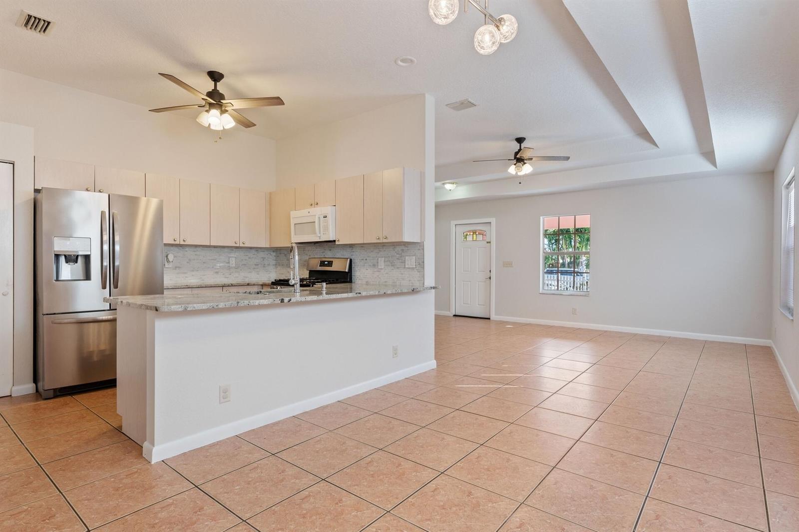 An open-concept kitchen with light wood cabinets and granite countertops overlooks a tiled living area — 623 N L Street, FL 33460, FL