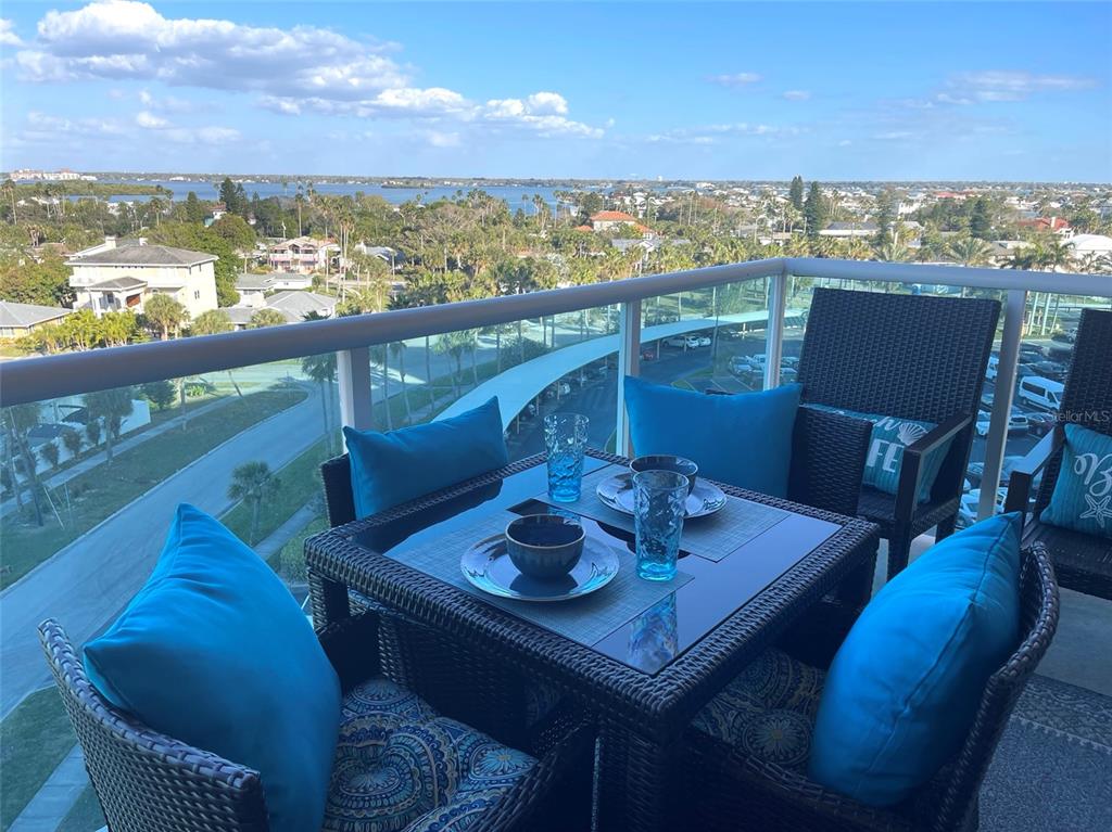 A balcony features a wicker dining set with blue cushions overlooking a coastal landscape — 880 MANDALAY AVENUE UNIT N610, CLEARWATER BEACH, FL
