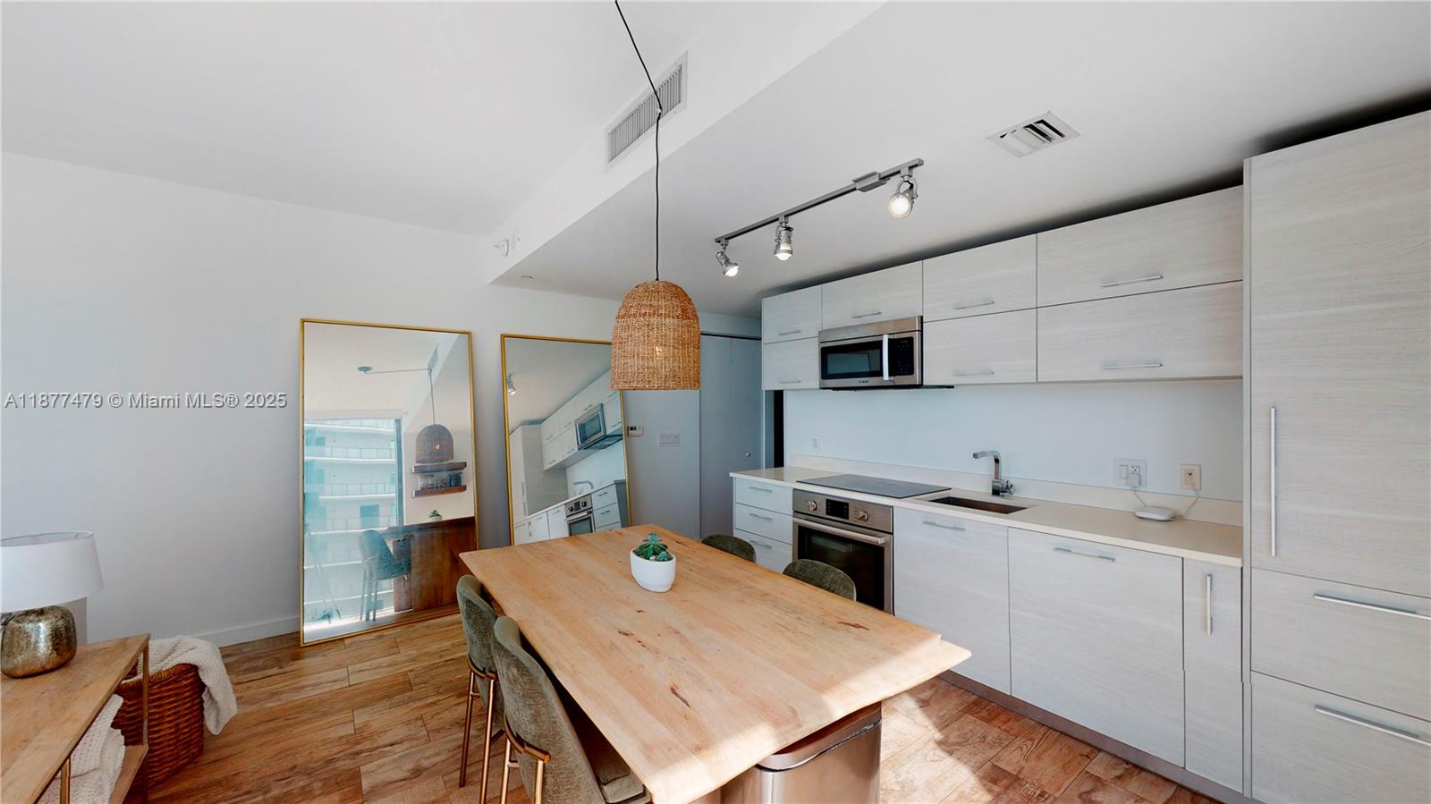 A modern kitchen features light wood cabinetry, a wooden dining table, and two large floor mirrors — 650 NE 32ND ST # 4607, Miami FL 33137, MIAMI, FL