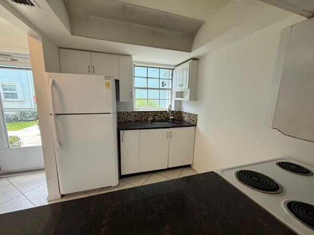 A kitchen features white cabinets, a white refrigerator, a dark countertop, and a window — 314 Waterside Drive, Hypoluxo FL 33462, HYPOLUXO, FL