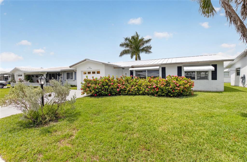 A white single-story house with a metal roof, a front lawn, and a flowering hedge — 719 SW 18TH STREET, BOYNTON BEACH, FL
