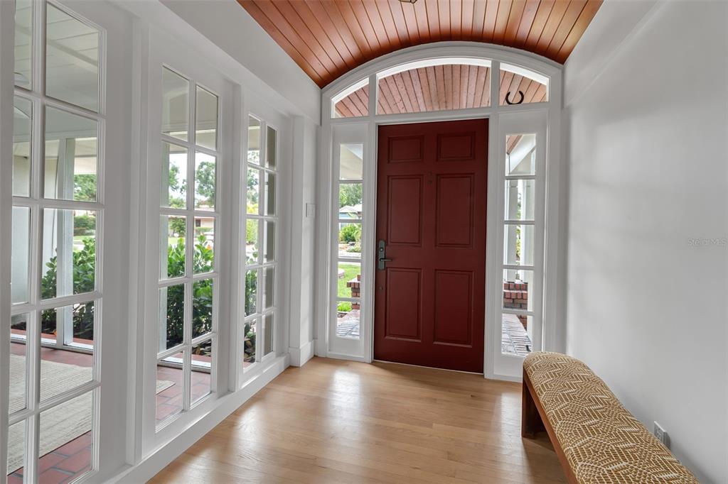 A bright entryway features a red door, wood-planked arched ceiling, hardwood floors, and glass panels — 1838 ALTA VISTA STREET, SARASOTA, FL
