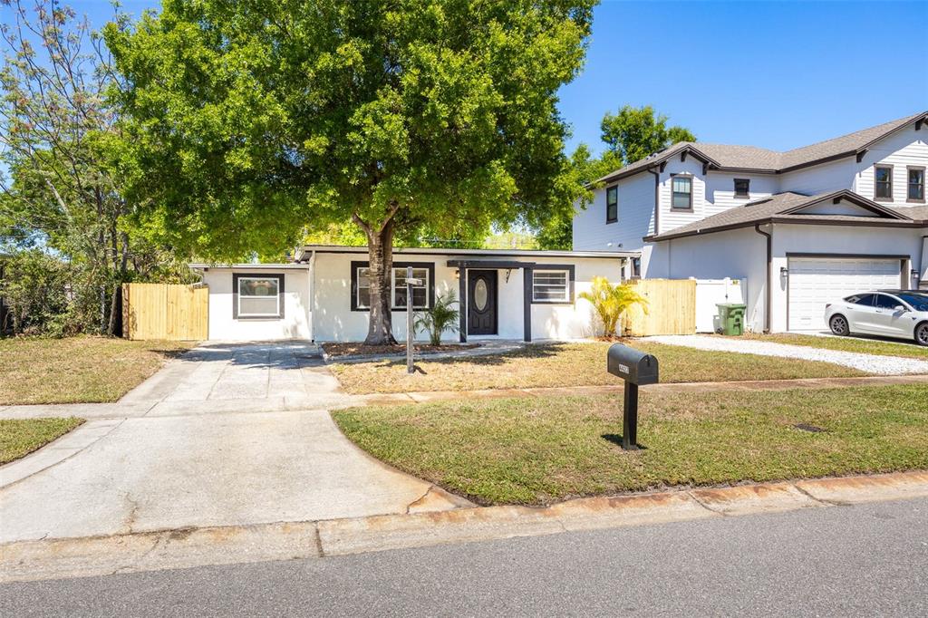 A single-story white house with a concrete driveway and a large tree in the front — 4427 W OKLAHOMA AVENUE, TAMPA, FL
