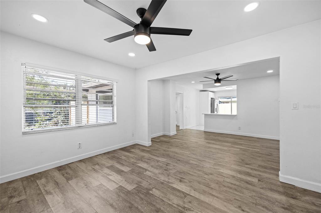 A living room with wood-look flooring, a ceiling fan, and an open kitchen beyond — 4427 W OKLAHOMA AVENUE, TAMPA, FL