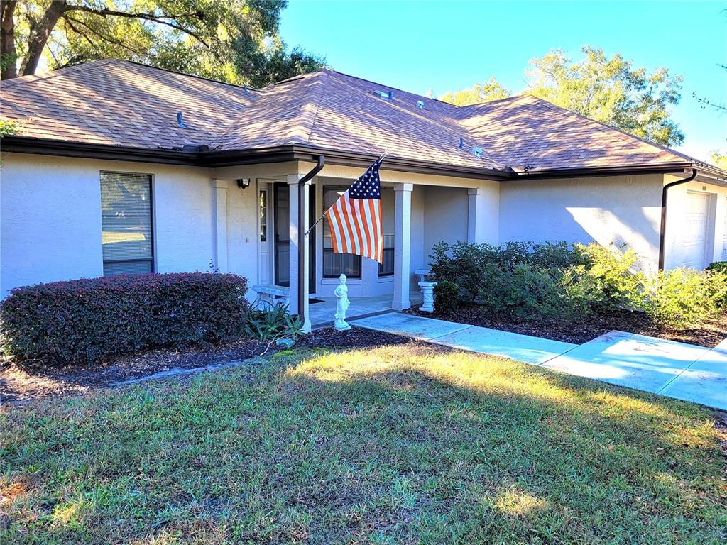 A single-story house with a tan stucco exterior, a shingled roof, and an American flag — 6018 W BROMLEY CIRCLE, CRYSTAL RIVER, FL
