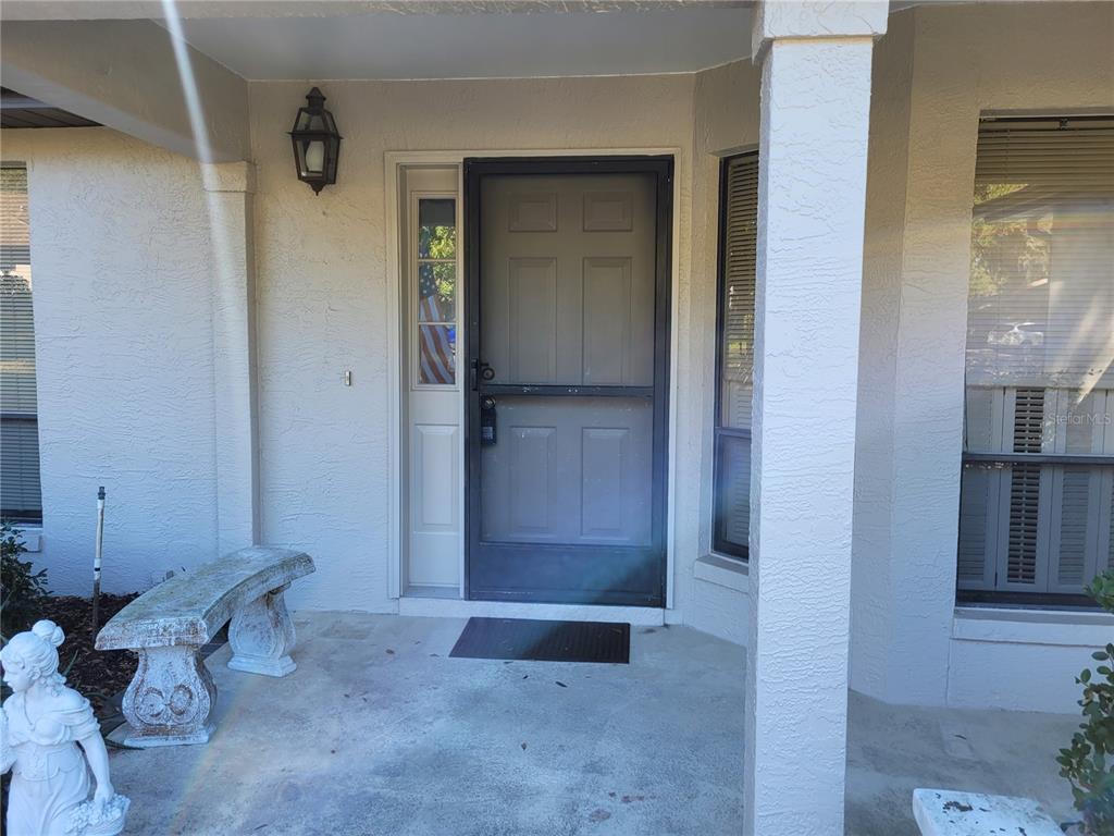 A covered front porch features a gray storm door, a stone bench, and a statue — 6018 W BROMLEY CIRCLE, CRYSTAL RIVER, FL