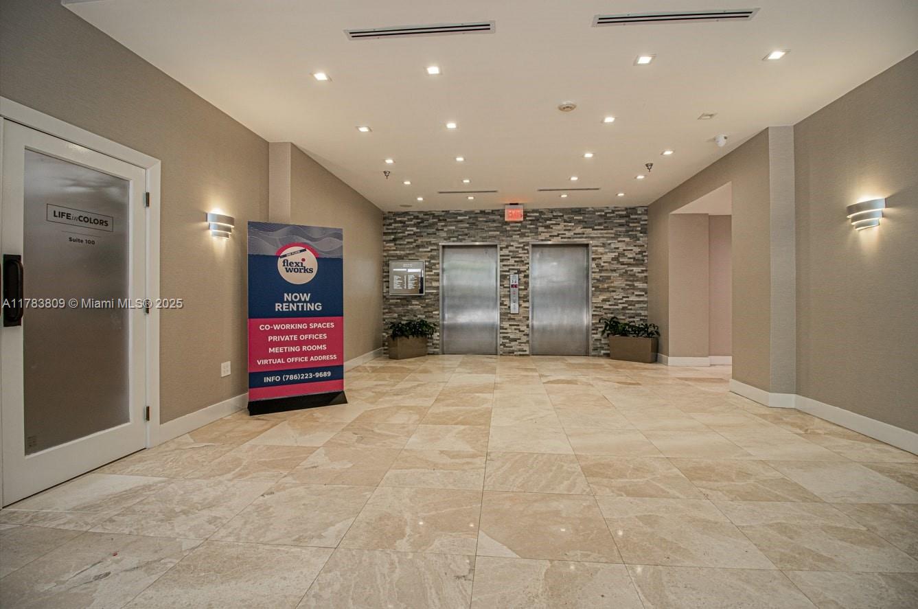 A modern office building lobby features stone tile flooring, two elevators, and a rental sign — 2100 SW 22nd St # 302, Miami FL 33145, MIAMI, FL