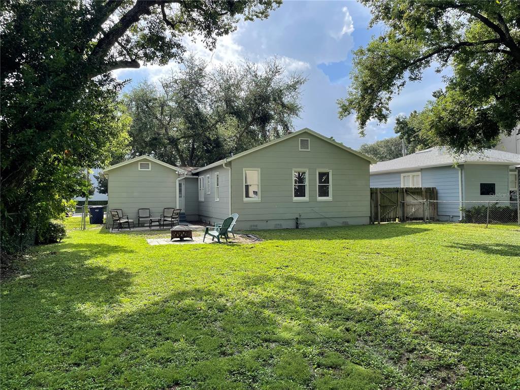The backyard of a light green house features a patio area with chairs and trees — 303 S AUDUBON AVENUE, TAMPA, FL