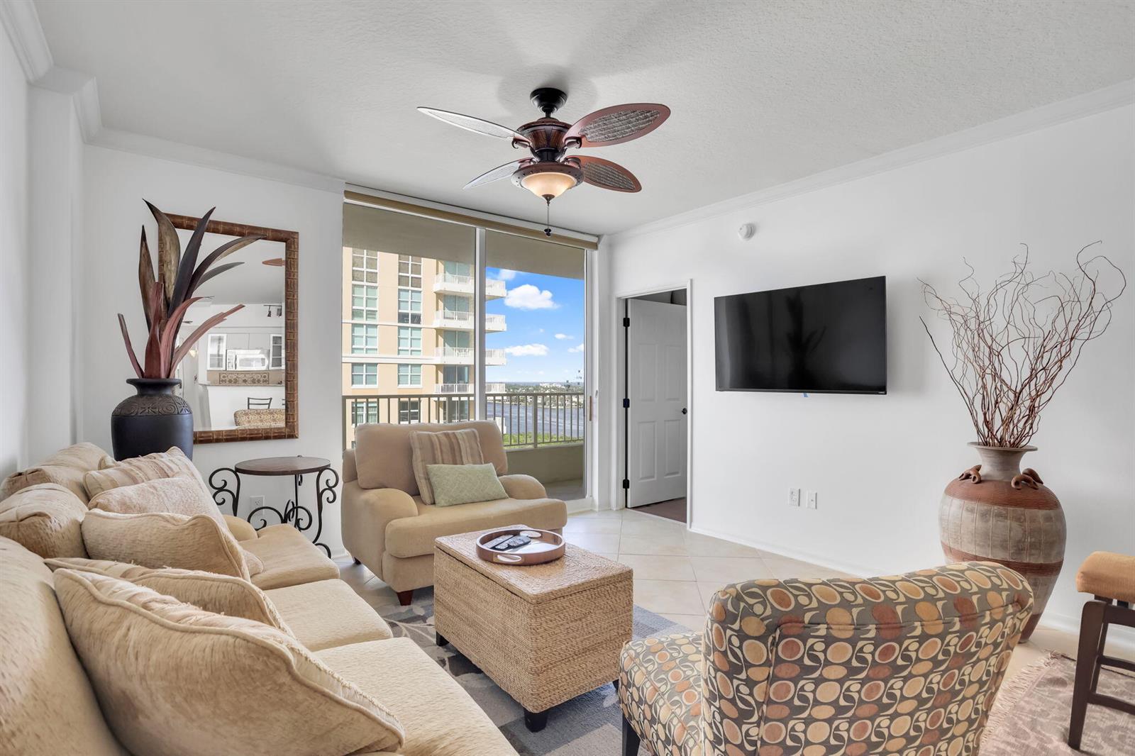 A living room features a beige sofa, patterned armchair, wicker ottoman, and a balcony view — 625 Casa Loma Boulevard # 1103, Boynton Beach FL 33435, BOYNTON BEACH, FL