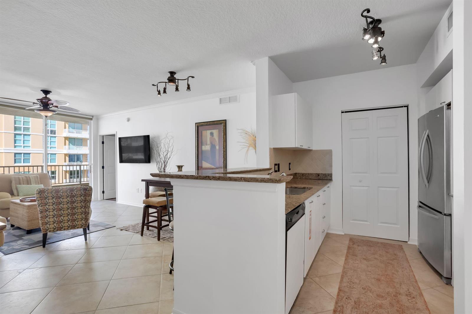 An open-concept kitchen and living area features tile flooring, granite countertops, and a balcony view — 625 Casa Loma Boulevard # 1103, Boynton Beach FL 33435, BOYNTON BEACH, FL