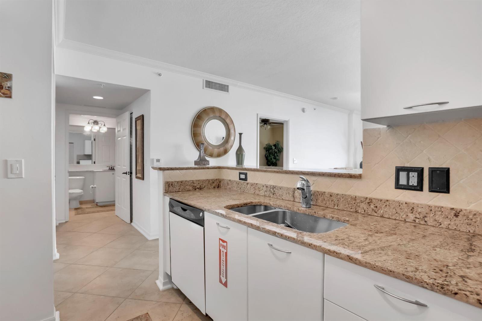 A kitchen features white cabinets, granite countertops, a double sink, and a pass-through window — 625 Casa Loma Boulevard # 1103, Boynton Beach FL 33435, BOYNTON BEACH, FL