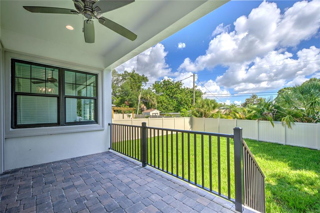 A covered patio with a paver floor, ceiling fan, and black railing overlooks a backyard — 855 39TH AVENUE N, ST PETERSBURG, FL