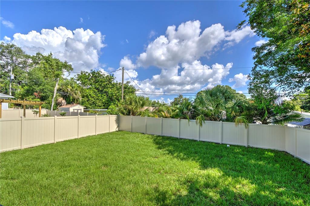 A grassy backyard enclosed by a tan vinyl privacy fence under a blue sky — 855 39TH AVENUE N, ST PETERSBURG, FL