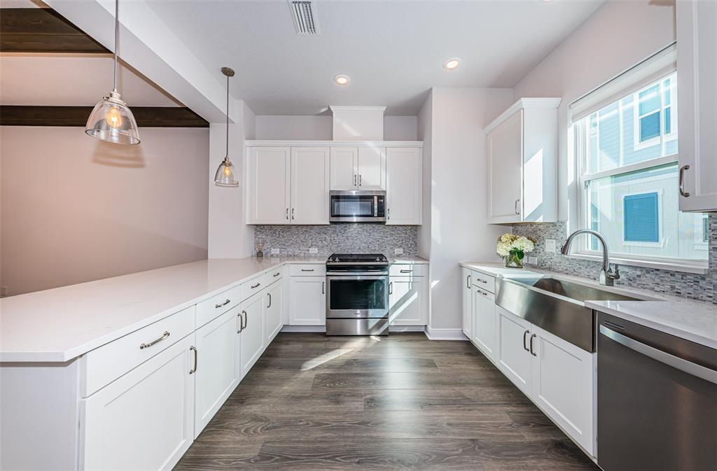 A modern kitchen features white cabinets, stainless steel appliances, a farmhouse sink, and wood flooring — 815 BURLINGTON AVENUE N, ST PETERSBURG, FL