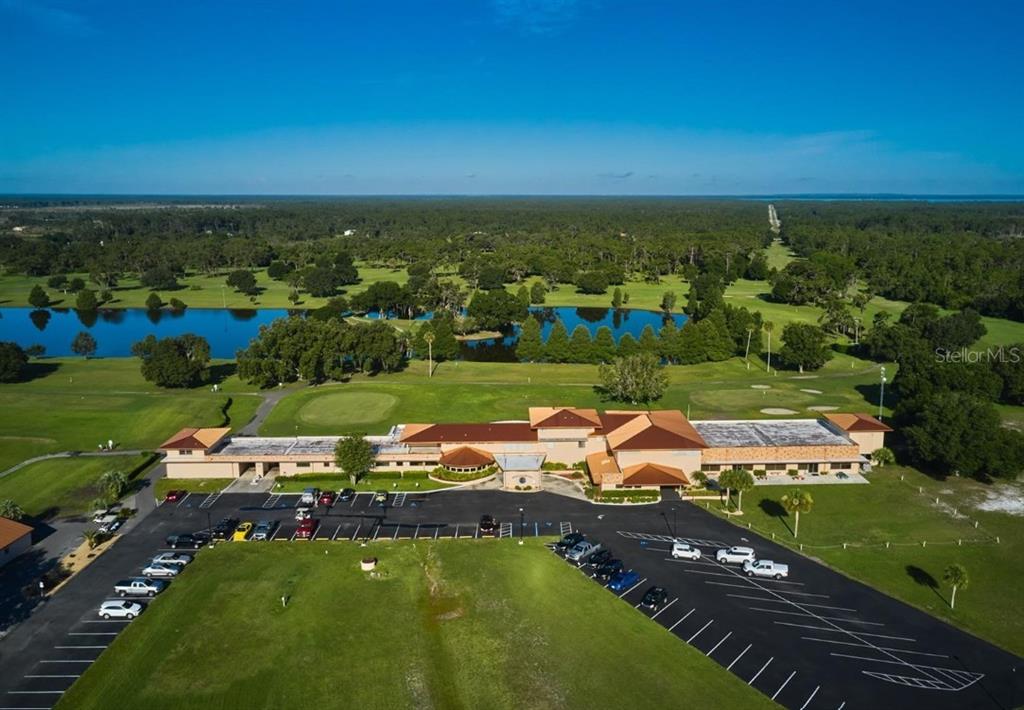 An aerial view shows a large clubhouse building with a parking lot and golf course — 515 GAILLARDIA DRIVE, INDIAN LAKE ESTATES, FL