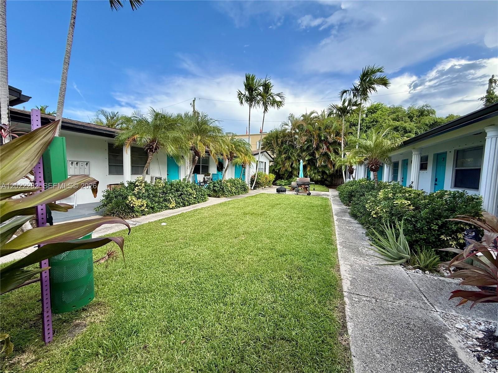 A grassy courtyard sits between two rows of single-story apartment units with palm trees — 3210 Canal Dr # 5, Pompano Beach FL 33062, POMPANO BEACH, FL