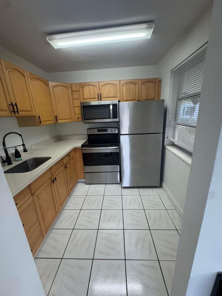 A galley kitchen features light wood cabinets, stainless steel appliances, and white tiled flooring — 3210 Canal Dr # 5, Pompano Beach FL 33062, POMPANO BEACH, FL