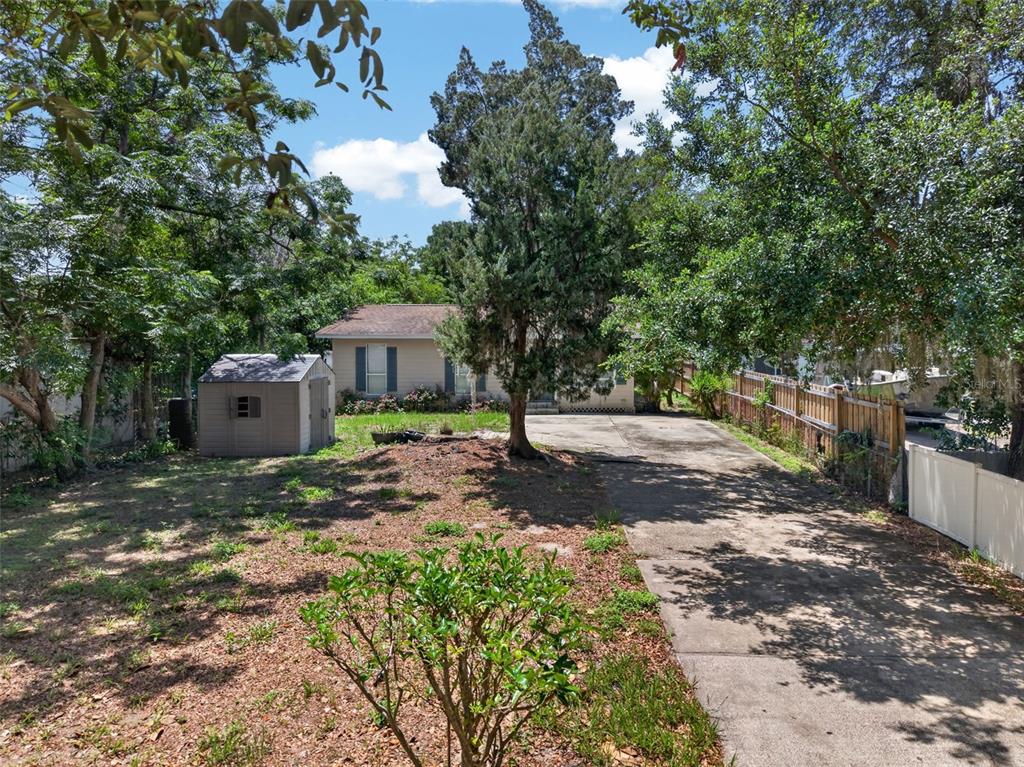 A tan house with a driveway, a storage shed, and mature trees in the yard — 4793 PLEASANT AVENUE, PALM HARBOR, FL