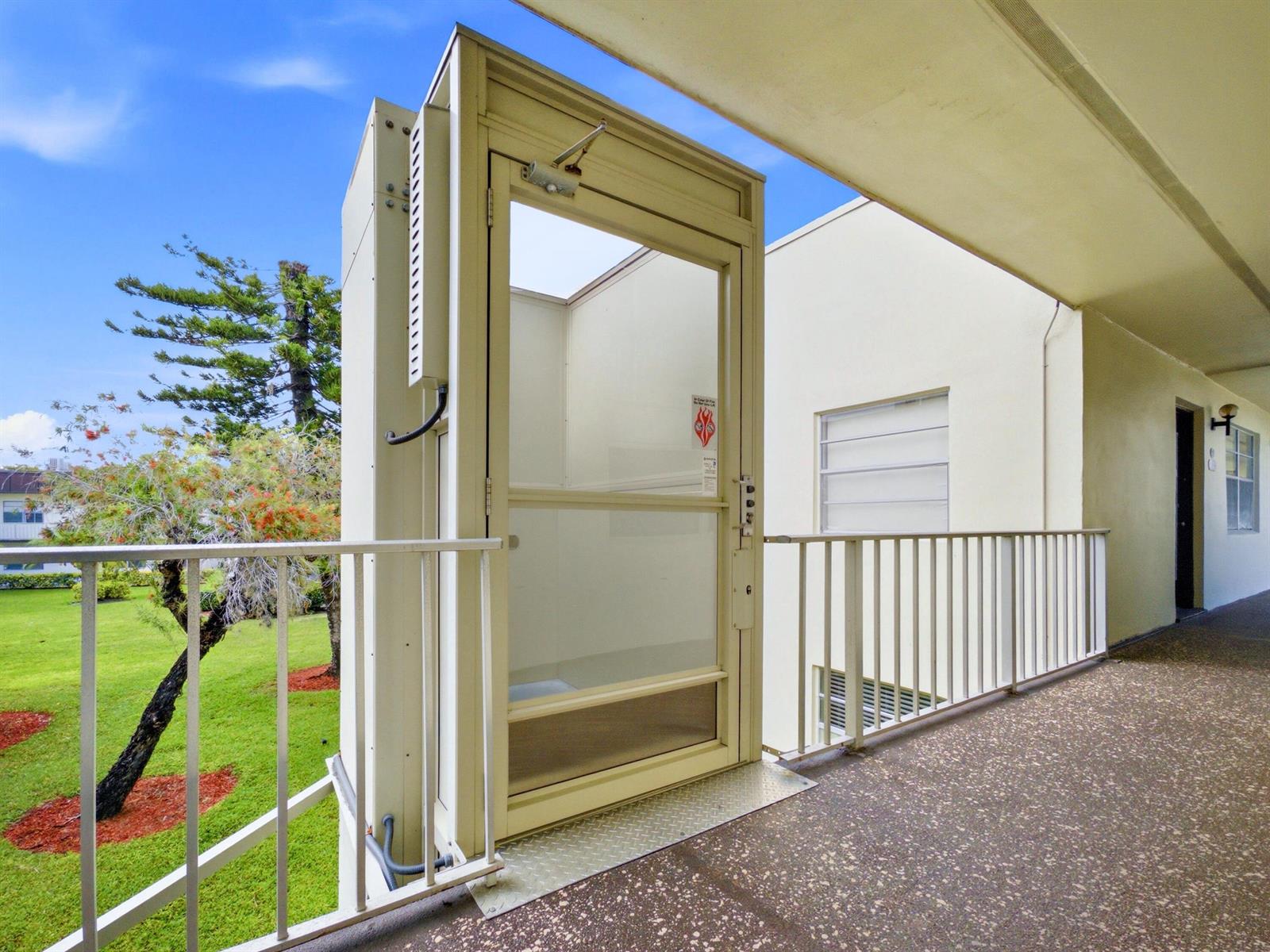 An outdoor wheelchair lift stands on a concrete balcony next to a white building — 755 Normandy P, Delray Beach FL 33484, DELRAY BEACH, FL