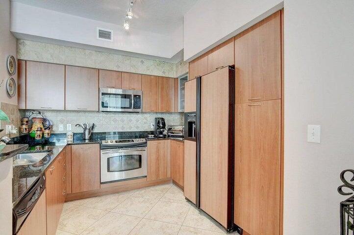 A kitchen features wood-toned cabinets, stainless steel appliances, and light-colored tile flooring — 625 Casa Loma Boulevard Unit 1, Boynton Beach FL 33435, BOYNTON BEACH, FL
