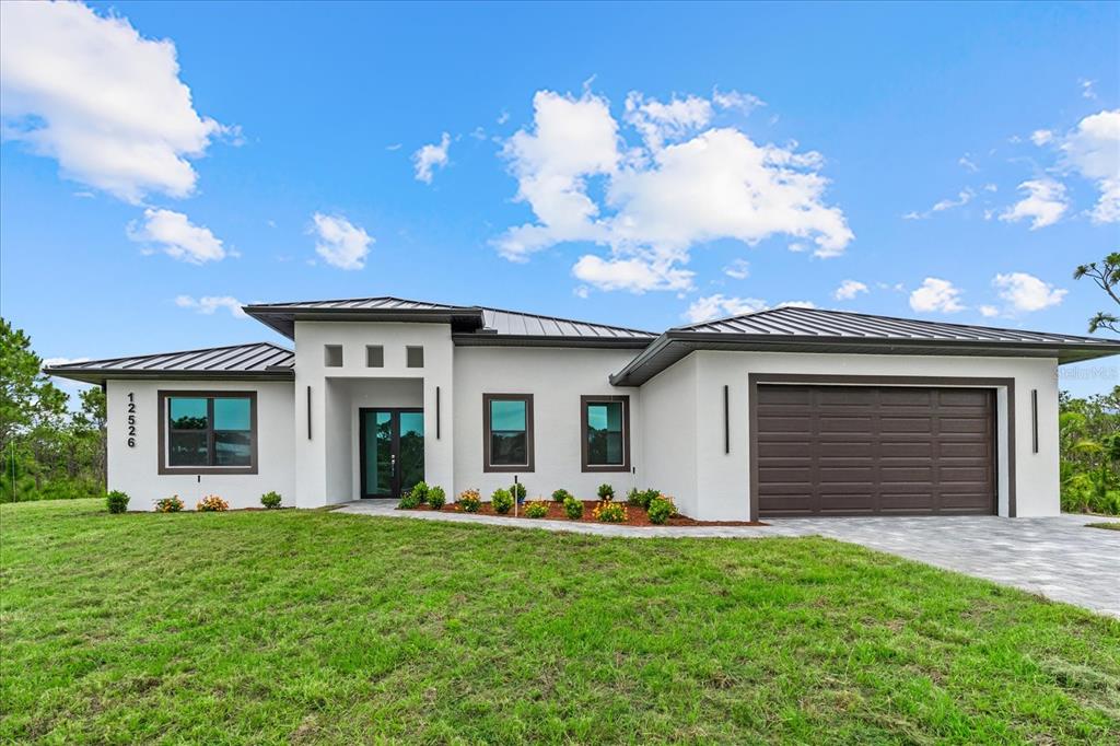 A modern single-story house with a white stucco exterior, dark metal roof, and attached garage — 12526 INDIAN SHELL TRAIL, BOKEELIA, FL