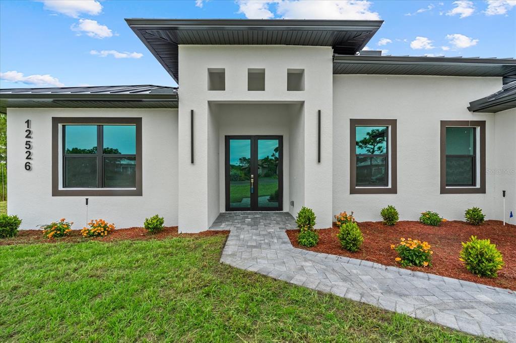 The exterior of a modern white house features a paved walkway and dark-framed windows — 12526 INDIAN SHELL TRAIL, BOKEELIA, FL