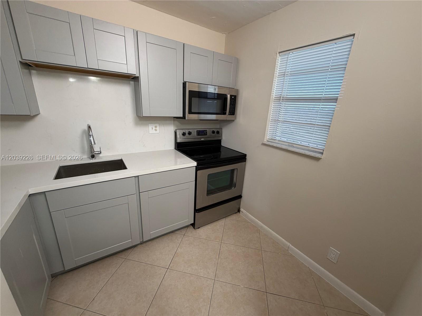 A kitchen features light gray cabinets, stainless steel appliances, white countertops, and tile flooring — 220 SW 9th Ave # 402, Hallandale Beach FL 33009, HALLANDALE BEACH, FL