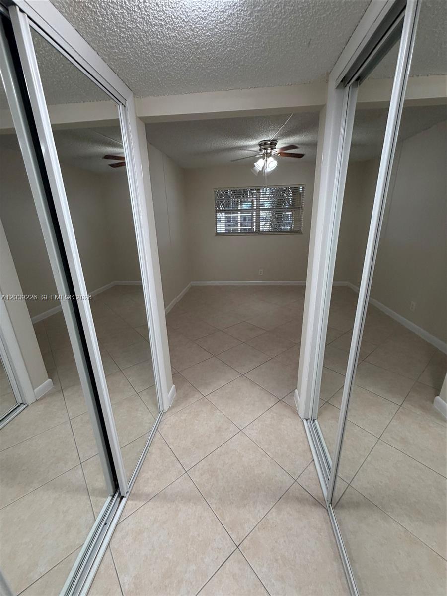 A room with beige tile flooring, mirrored closet doors, and a ceiling fan — 220 SW 9th Ave # 402, Hallandale Beach FL 33009, HALLANDALE BEACH, FL
