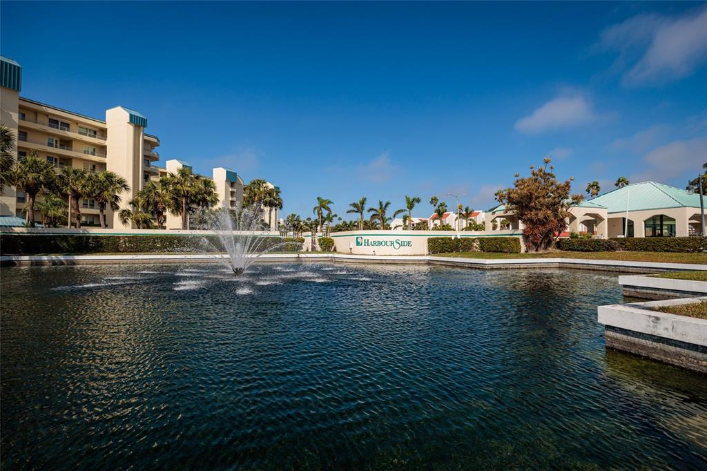 A fountain sits in a pond in front of a multi-story building labeled Harbourside — 7897 SAILBOAT KEY BOULEVARD UNIT 107, SOUTH PASADENA, FL