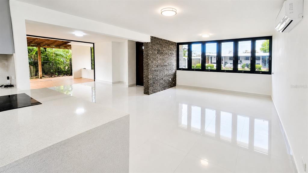 A bright, open-concept living area features white tile floors, a stone accent wall, and windows — Urb Parkville AVE. LOPATEGUI, GUAYNABO, PR