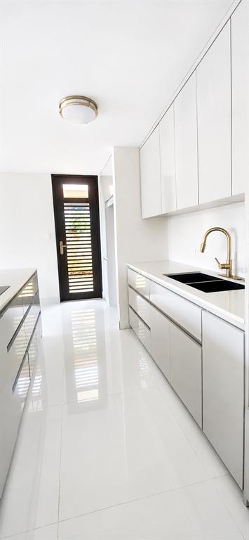 A modern kitchen features white glossy cabinets, a gold faucet, and a dark slatted door — Urb Parkville AVE. LOPATEGUI, GUAYNABO, PR