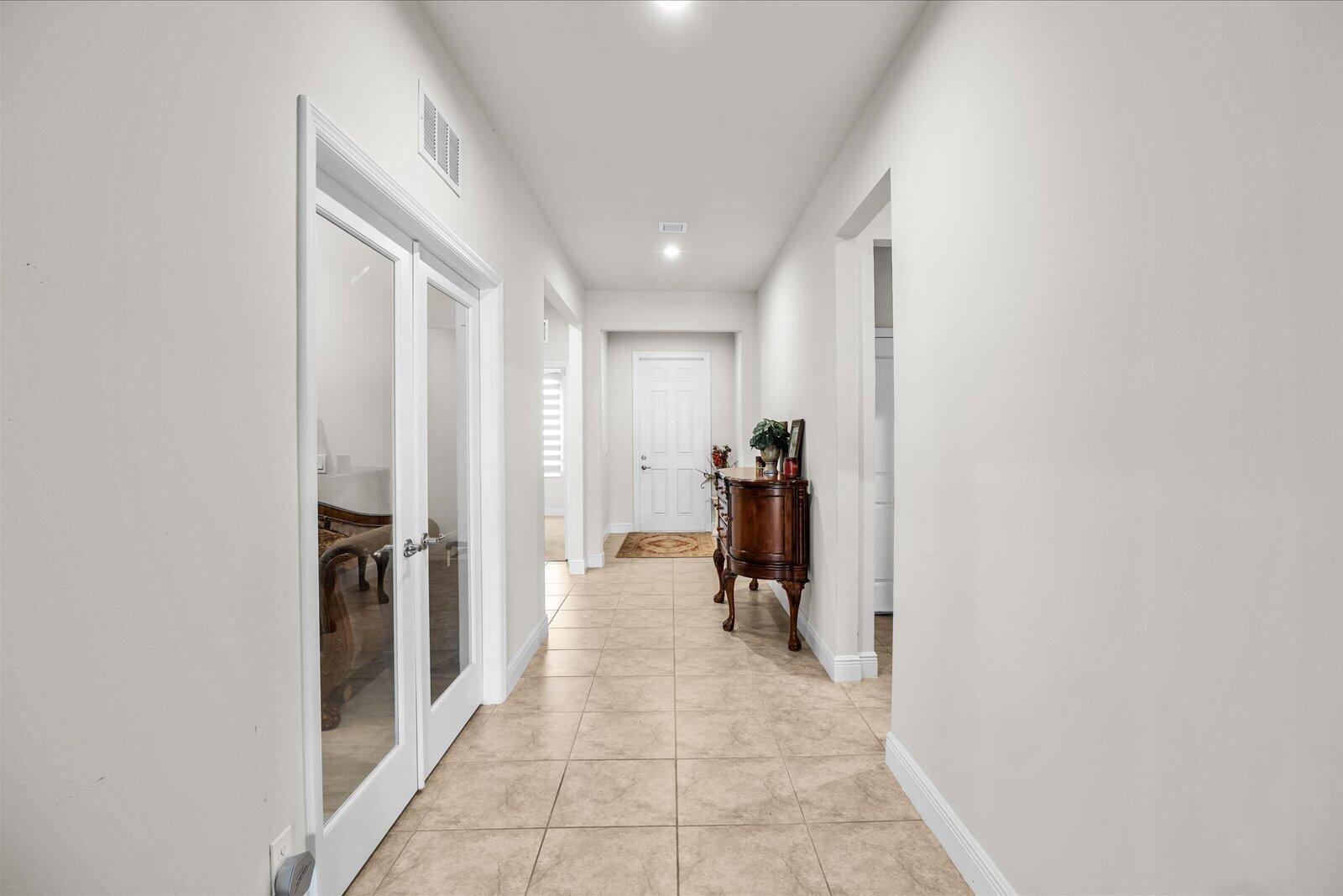 A hallway with tile flooring leads to a white door and a wooden console table — PORT ST. LUCIE, FL